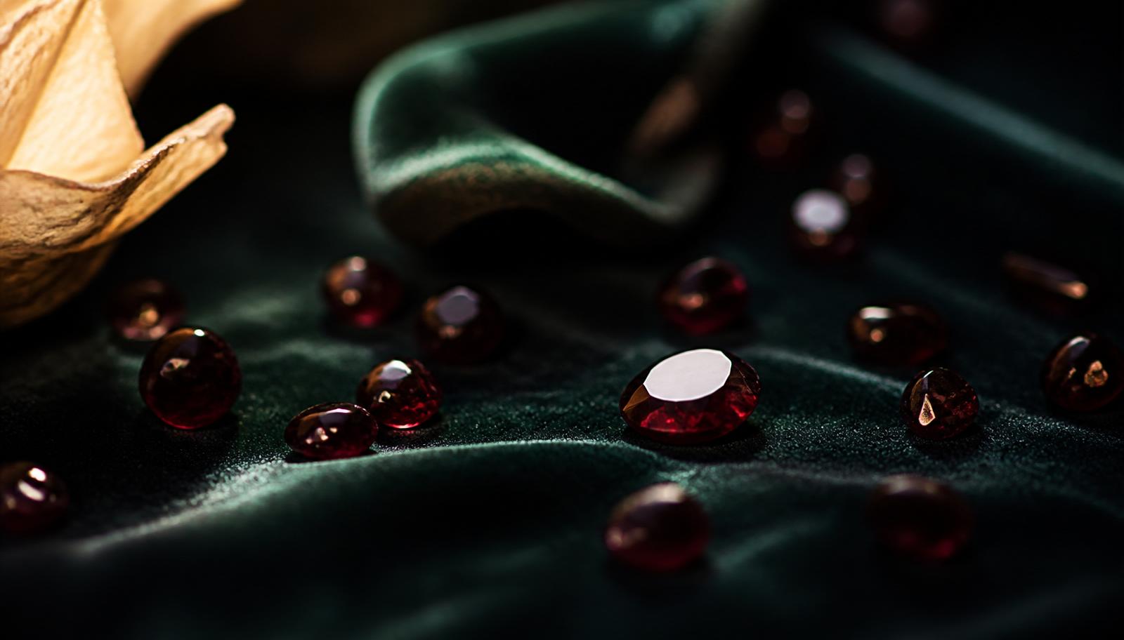 Loose wine-red garnets in various cuts and one rough crystal on bottle-green velvet — atmospheric image, not a determination example.
