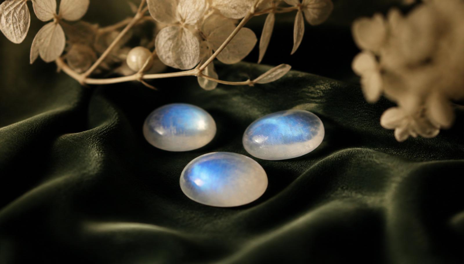 Two moonstone cabochons with soft blue Schiller on bottle-green velvet — atmospheric image, not a determination example.